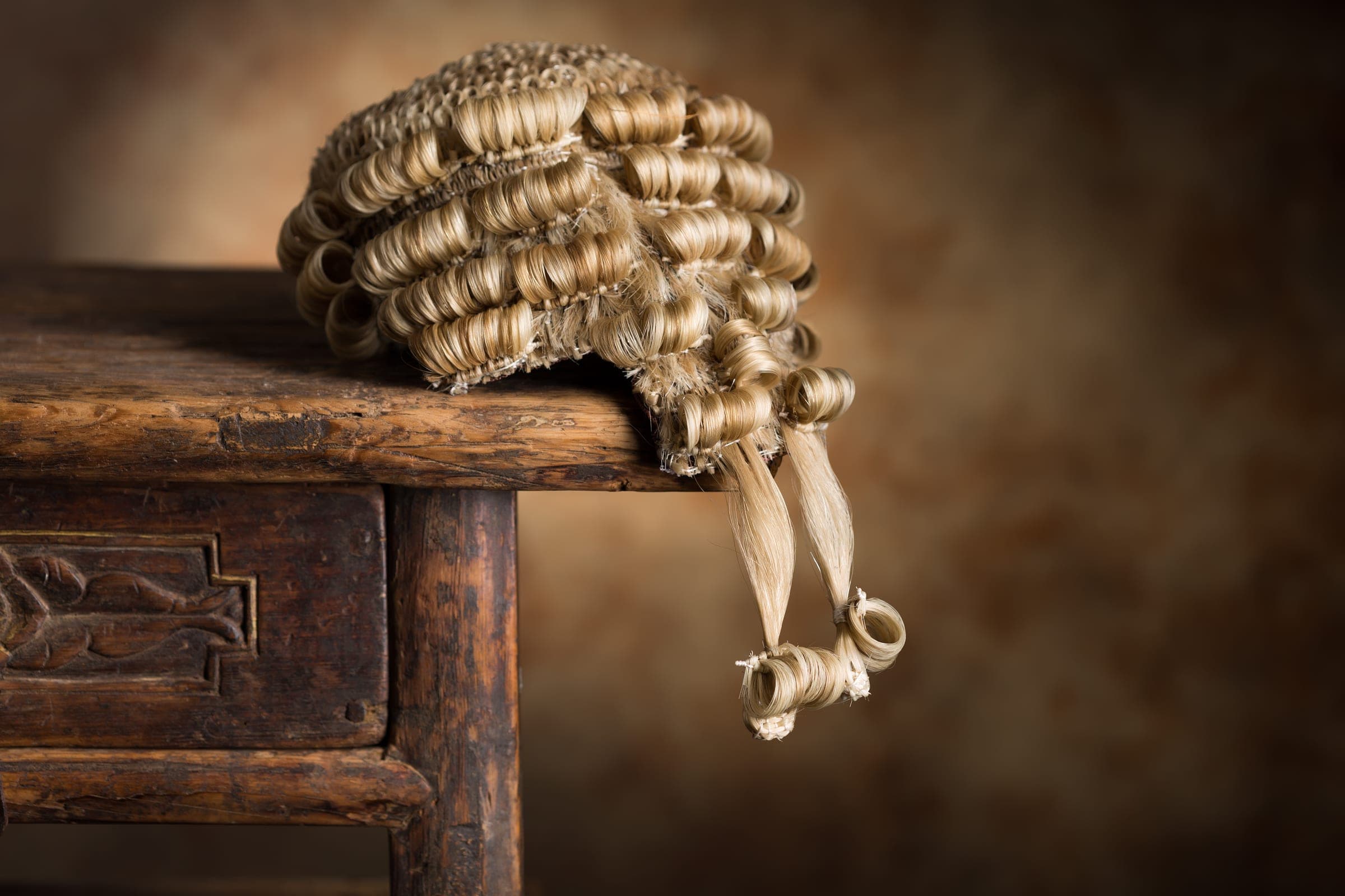 A barrister's wig resting on an antique wooden bench.