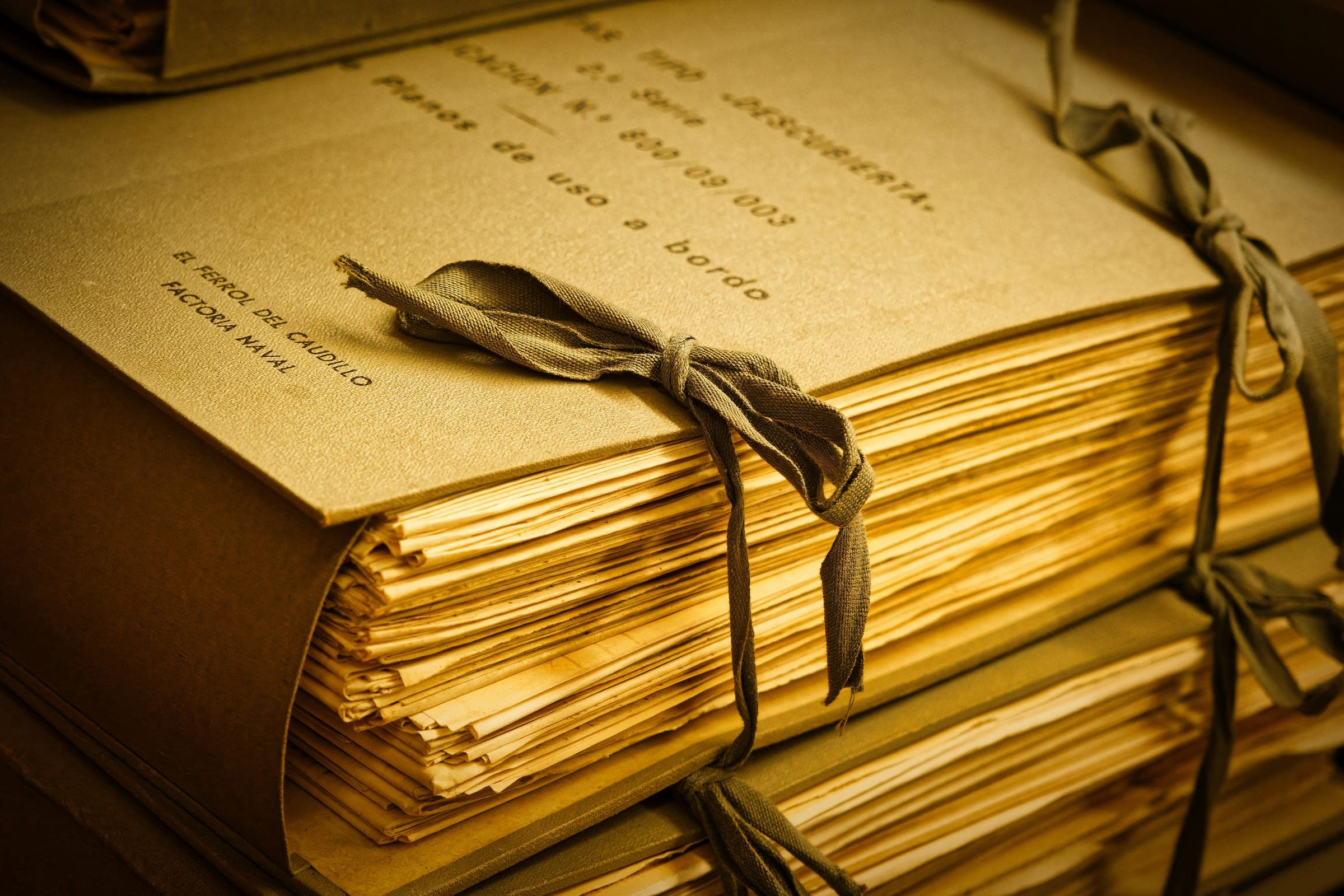 Stacked bundles of papers tied with ribbon, lit by golden light.