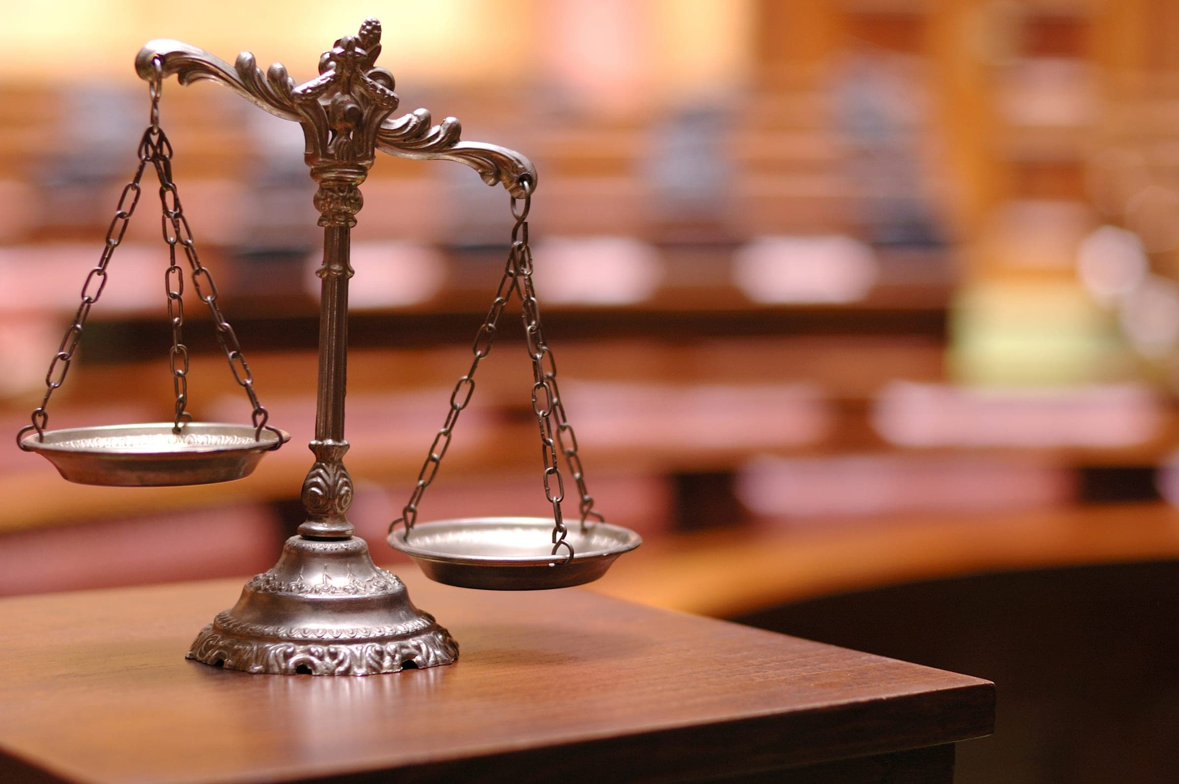 Scales of justice on a desk in an empty courtroom.